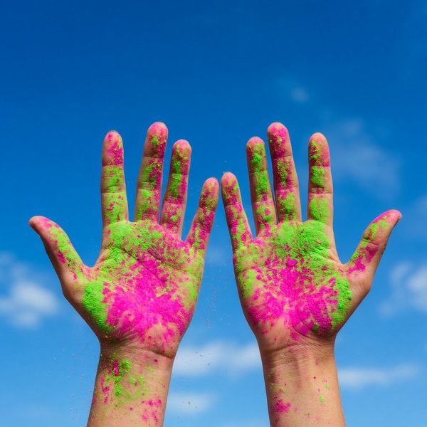 Coloured Hands Holi DP – Two raised hands covered in bright pink and green colour powder against blue sky. A free HD holi DP for WhatsA… (Holi DPS)